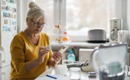 starsza pani w kuchni z pojemnikiem leków i komórką w rękach