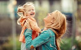 Matka trzyma w górze roześmianą pięciolatkę z kucykami