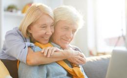 50letnia pani obejmuje za szyję męza, on patrz w laptop