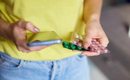 ktoś ma w jednej ręce telefon, w drugiej blistry lekow