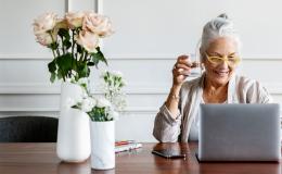 Starsza pani w koku przed laptopem, na stoliki w wazonach dwa bukiety: róże i goździki