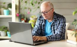 Starszy, siwy pan we flanelowej koszuli przed komputerem