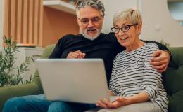 Para 50latków z laptopem na kanapie, on ją obejmuje ramieniem 