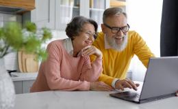 Para w średnum wieku z uśmiechem zagląda do laptopa