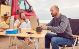 para przed kamperem, mężczyzna przy laptopie, w tle plaża