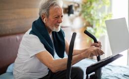 Starszy pan na orbitreku i z laptopem