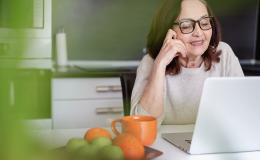 Kobieta ok 60ki przed laptopem, obok niej taca z pomarańczami