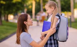 mama kuca i trzyma za ręce córkę z tornistrem, patrza na siebie z uśmiechami