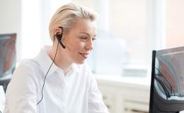 Pani w białej bluzce ze słuchawkami w uszach przed komputerem