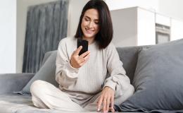 Kobieta na kanapie siedzi po turecku, ma komórkę