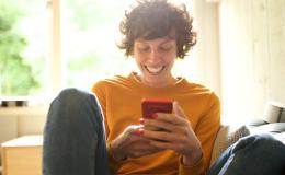 Roześmiana dziewczyna trzyma w ręku telefon i patrzy na ekran