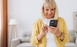 Seniorka z komorka w domu, w rozpiętym swetrze