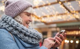 starsza pani w cieplej czapce na dworze, z komórką w reku