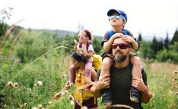 łąka z wysoką trawą, rodzice niosą dzieci na barana