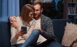 Przytulona para na kanapie, ona trzyma w ręku komórkę