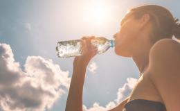 Kobieta pije wodę z butelki, w tle słoneczne niebo
