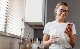 Dziewczyna w białym t-shircie ze szklanką wody i komórką w kuchni