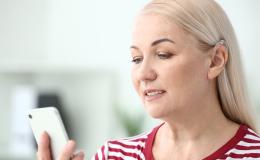 Blondynka z aparatem słuchowym patrzy na telefon 