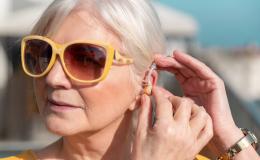 kobieta z aparatem słuchowym, w ciemnych okularach, siwe włosy