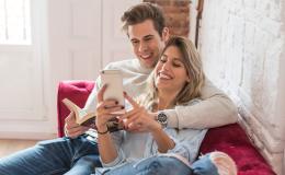 para siedzi wtulona na kanapie, on z ksiazka, ona z komórką mu coś pokazuje z uśmiechem