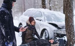 śnieg, wypadek samochodowy, jedna osoba trzyma komorke, druga udziela pomocy poszkodowanemu