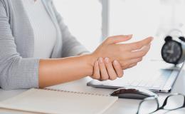 kobieta przy komputerze trzyma się za rękę