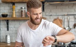 Młody mężczyzna w kuchni patrzy na zegarek