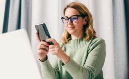 30latka z komórką, na którą patrzy, przed nią laptop