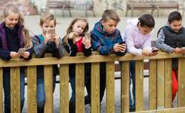 dzieci stoją przy płocie i patrzą w telefony
