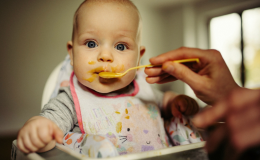 Dziecko siedzi w krzesełku dla dzieci i jest karmione łyżeczką