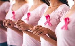 Kobiety w różowych koszulkach z przyczepionymi różowymi wstążkami stoją i trzymają się za ręce.