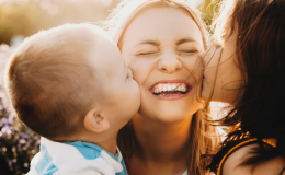 Dwoje dzieci całuje w policzki uśmiechniętą mamę