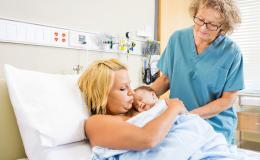 Kobieta lezy z noworodkiem, stoi położna