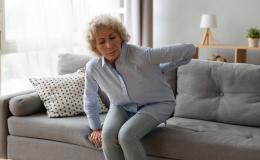 starsza pani z trudem siada na kanapie