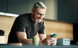 Pan z komórką w ręku, oparty łokciami o stół w kuchni