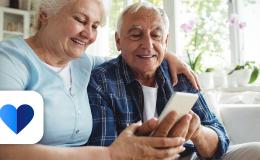 Starsza para na kanapie, żona pokazuje coś męzowi na komórce