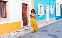 kobieta w żółtej sukience na tle biało-żółtego i bialo-niebieskiego domu, z komórką