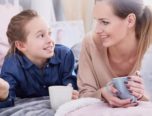 Mama i córka leżą na łóżku z herbatą i rozmawiają