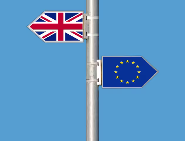 Na niebieskim tle maszt z zamocowanymi dwoma flagami. Z lewej strony flaga Wielkiej Brytanii. Z prawej strony i niżej flaga Unii Europejskiej.