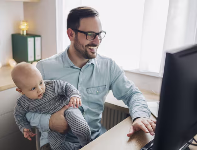 Tata z niemowlęciem na ręku przed komputerem