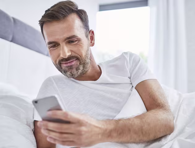 Leżący w łóżku facet patrzy na swój telefon