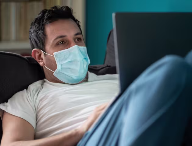 Mężczyna leży na kanapie z laptopem na kolanach i umawia się na test covid przez internet.