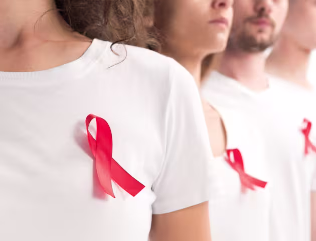 Osoby w białych koszulkach z przypiętą do piersi czerwoną wstążeczką