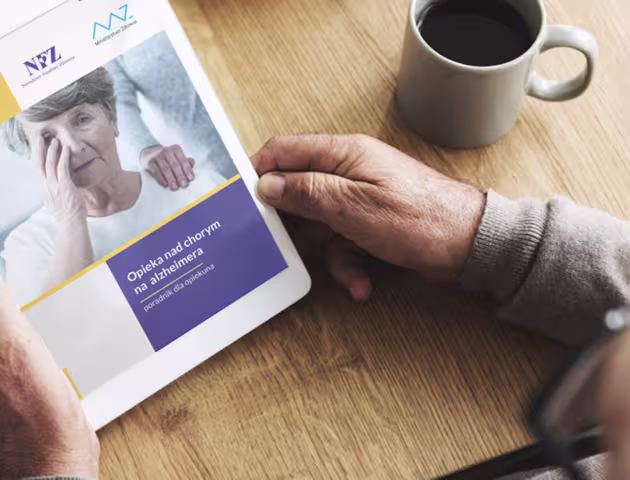 Mężczyzna trzyma w rękach tablet. Ma na nim wyświetlony poradnik dla opiekunów nad chorym na alzheimera 