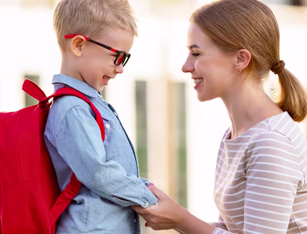 mama trzyma dziecko za obie ręce, kucając, chłopiec w okularkach śmieje się