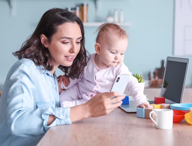 Mama z dzieckiem przy stole. Mama przegląda telefon, a dziecko bawi się klockami.