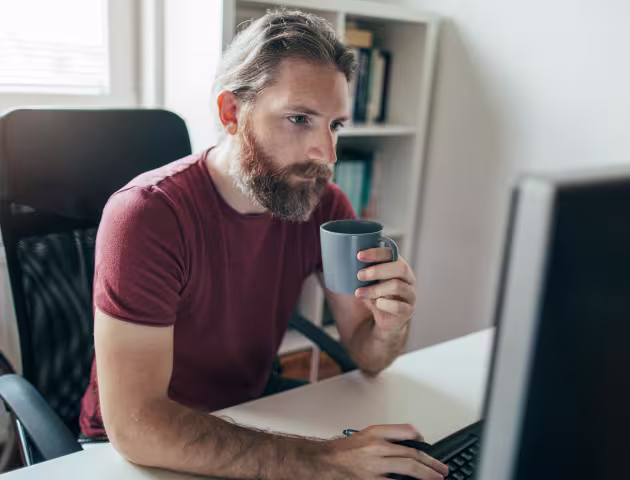 Brodaty mężczyzna z kubkiem przed laptopem