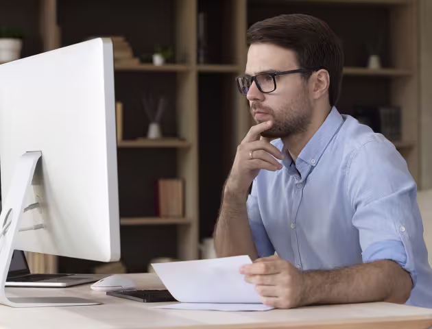 Mężczyzna z papierami przed komputerem
