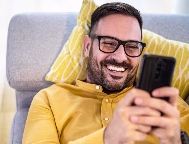 Mężczyzna w żółtej koszuli leży na kanapie z telefonem