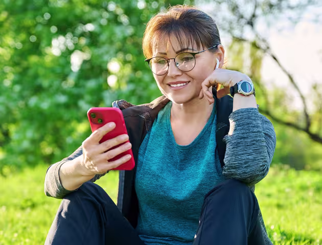 Pani siedząca na trawie z uśmiechem patrzy na telefon
